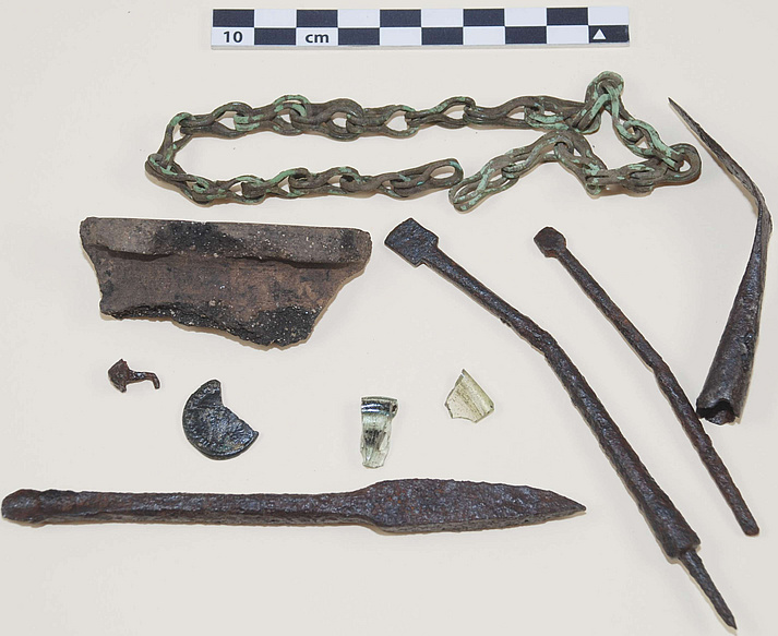 Assembly of finds from a road (400-600 AD) during the 2012 campaign: bronze chain, iron arrowhead, fragment of coarse pottery, two iron styluses, shoe nail, late Roman coin, two glass fragments, iron spoon auger  